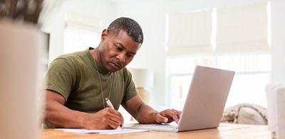 Working at home, the serious mature adult soldier takes continuing education courses online using his laptop.