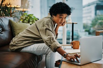 Cropped shot of a young woman using her laptop while sitting with her notebook at home