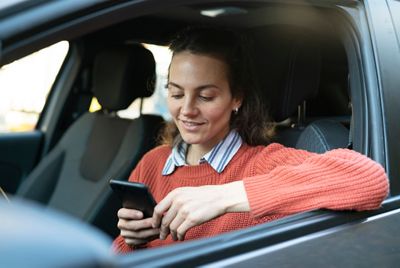 Smiling beautiful male mature adult using smart phone while sitting inside of a car during daytime