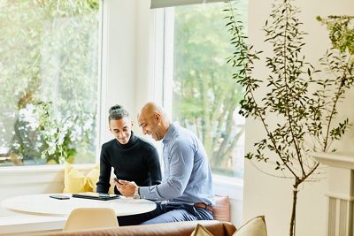 Medium wide shot of smiling father and son looking at app on smart phone while sitting in living room