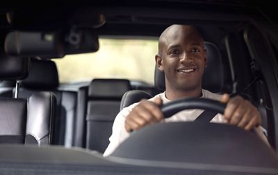 Portrait of a happy African American man driving a car and smiling - shot through windshield concepts