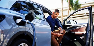 Man using smart phone sitting in car getting charged at station