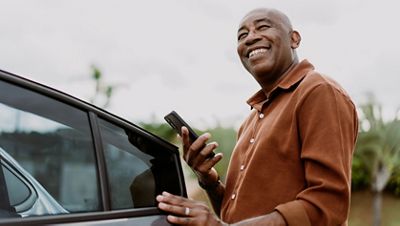 Man getting into car holding smartphone