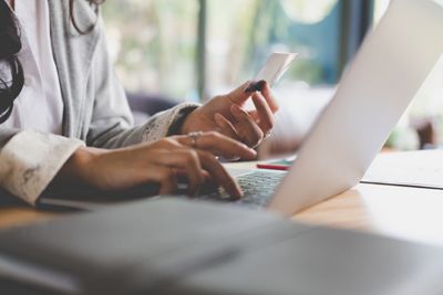 young woman holding a credit card and using laptop computer for online shopping at cafe. businesswoman purchase goods from internet at office. female adult make payment on bank website at workplace