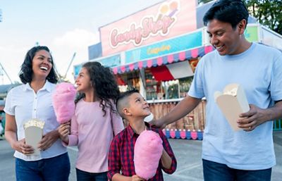 Portrait of a happy family having fun at a amusement park eating popcorn and candy cotton - lifestyle concepts