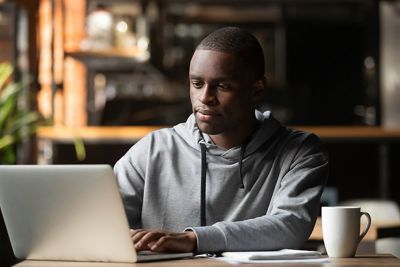 African American man using laptop in cafe, looking at screen, typing on keyboard, chatting in social networks with friends, writing post or report, message, working on project, surfing internet