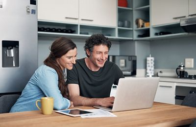 Shot of a couple using a laptop while going through paperwork together at home