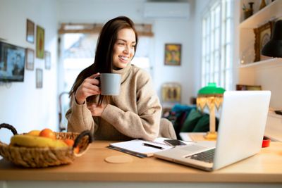 Smiling young woman freelancer working at home, using a laptop and drinking coffee