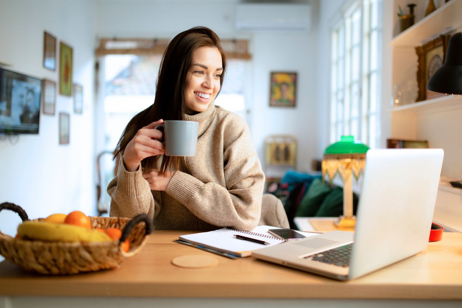 Smiling young woman freelancer working at home, using a laptop and drinking coffee