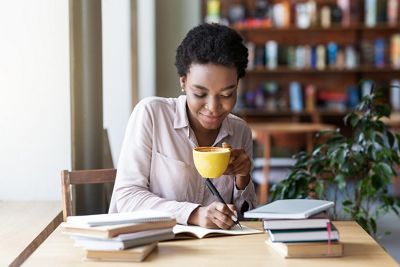 Beautiful black girl taking notes during her studies at coffee shop. Panorama