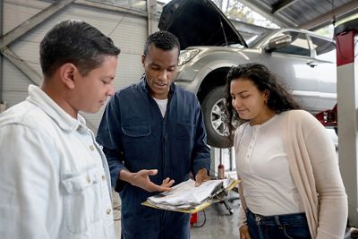 Mechanic talking to a couple about how to fix their car at an auto repair shop - vehicle breakdown concepts