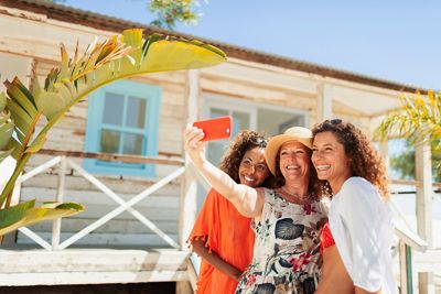Happy mother and adult daughters taking selfie outside sunny beach hut