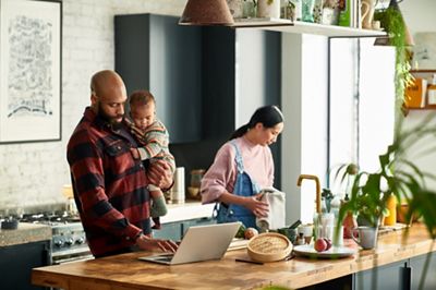 Black father holding baby son and using laptop, watching cooking video online, modern family life, real people