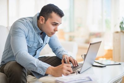 Young man sitting on the couch at home on a laptop doing finances.