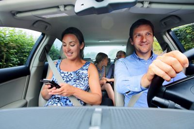 Mom reading text on phone while family on a car trip