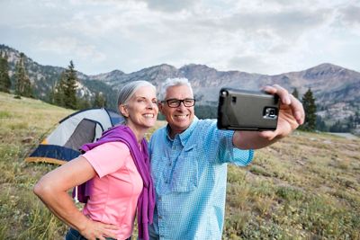 Caucasian couple posing for cell phone selfie on mountain