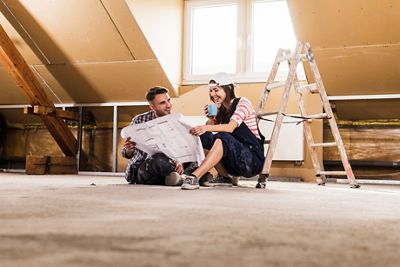 A woman holding up two choices of carpet fabric to a man in the kitchen