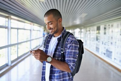 Shot of a young man using a mobile phone in a corridor on campus