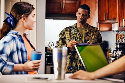 Friends in kitchen having coffee and on the laptop