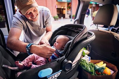 Dad strapping baby into car seat after loading groceries.