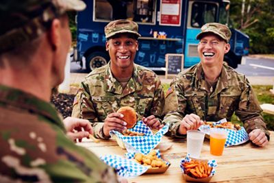 Military comrades laughing during conversation while having lunch together outside
