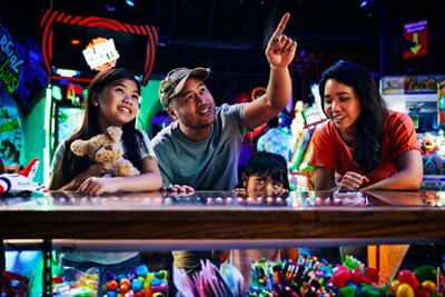 Father points out prizes to daughters in arcade booth as mom looks on