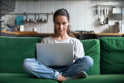 Serious woman using laptop checking email news online sitting on sofa, searching for friends in internet social networks or working on computer, writing blog or watching webinar, studying at home; Shutterstock ID 1156208407; Purchase Order: -