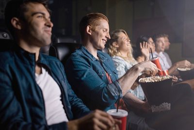 Young man with friends watching movie in cinema. Group of people in theater with popcorn and drinks.; Shutterstock ID 514155400; purchase_order: -; job: -; client: -; other: -