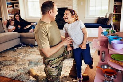 Military father and daughter laughing in the living room while mother watches